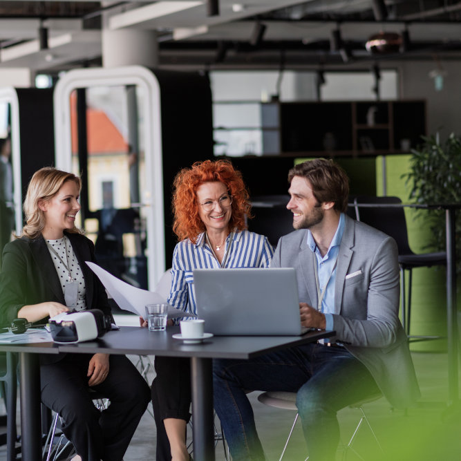 Three business professionals having a friendly meeting around laptop in modern office with bright collaborative workspace