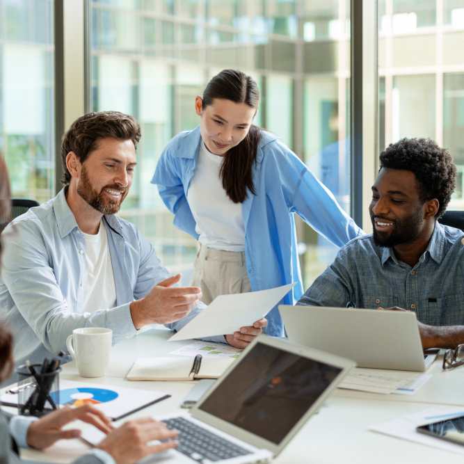 Three business professionals collaborating over documents in a bright modern office with laptops and coffee