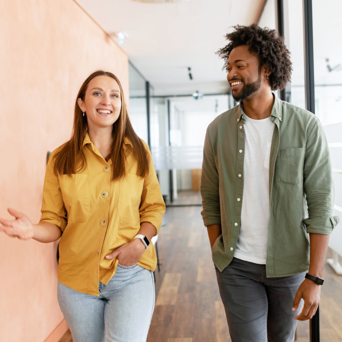 Two smiling business professionals walking together through modern office with bright natural lighting