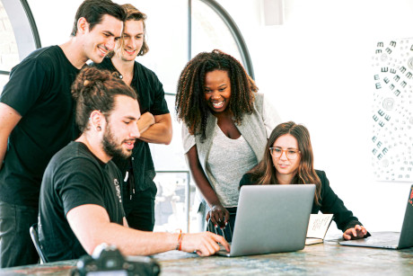 Group of colleagues gathered around desk reviewing work on laptop together in contemporary office