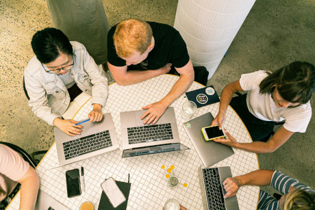 Team working together around a table with laptops, notebooks, and phones during a collaborative meeting