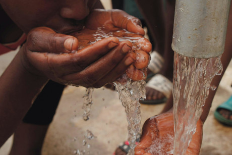 Person drinking fresh water from a hand pump