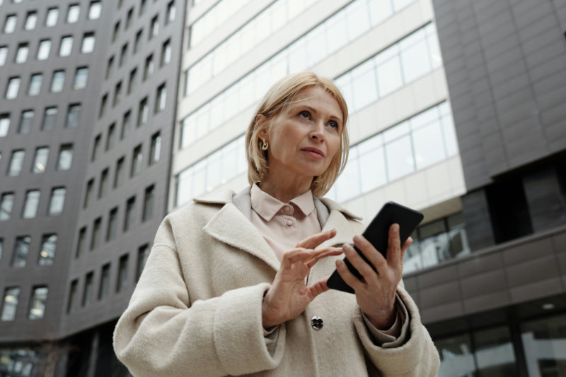 Business professional using smartphone while standing outside modern corporate office building