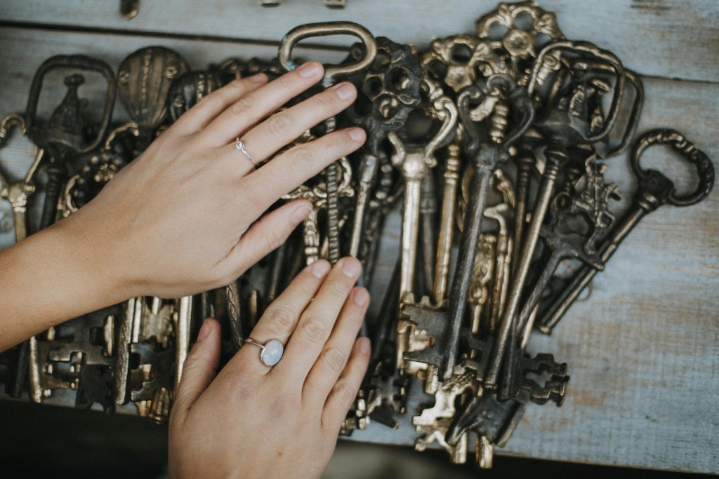 Hand displaying rings over a collection of ornate vintage brass keys on a wooden surface.