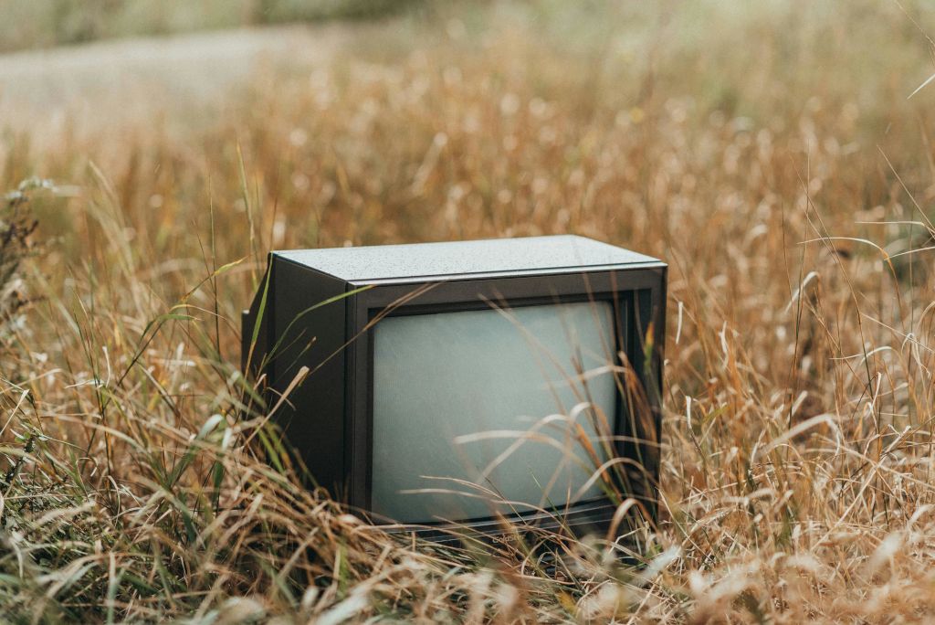 Old television set abandoned in a dry, overgrown field.