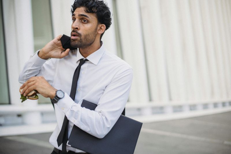 A busy man in a professional attire holding a sandwich and a file.