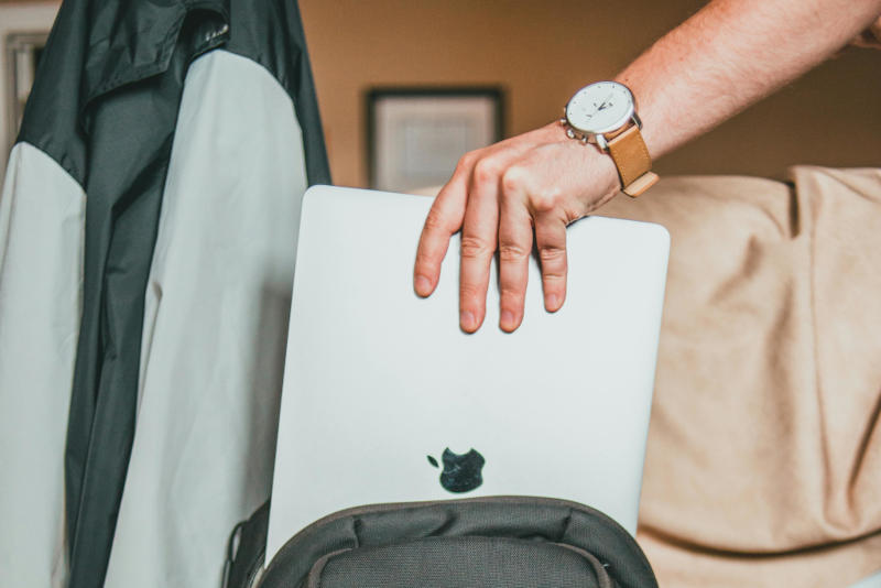 A person taking a closed laptop from a backpack in a home or office setting.