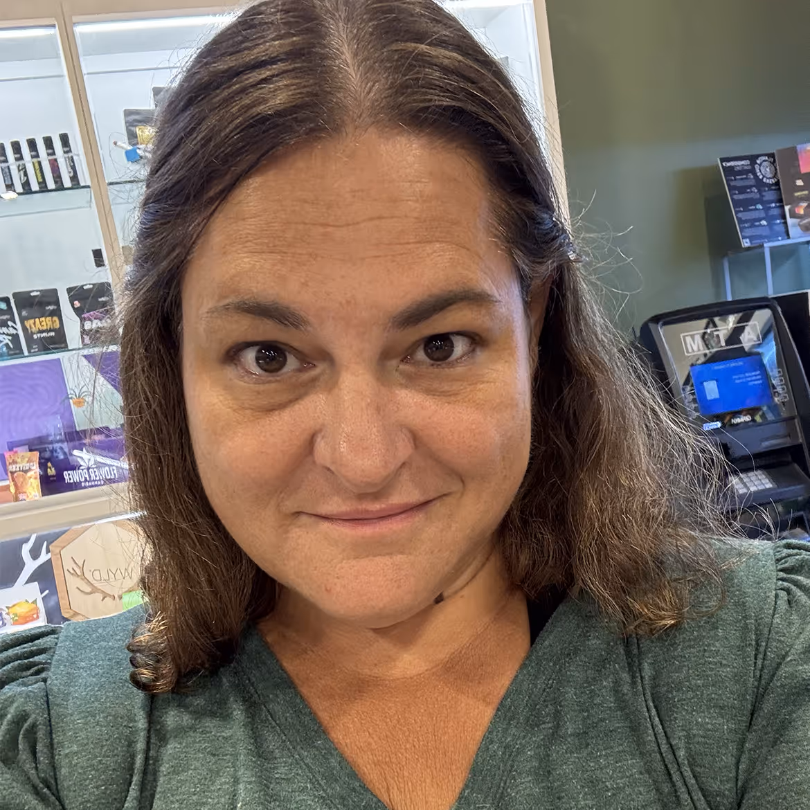 Woman smiling in store with product shelves and cash register behind her