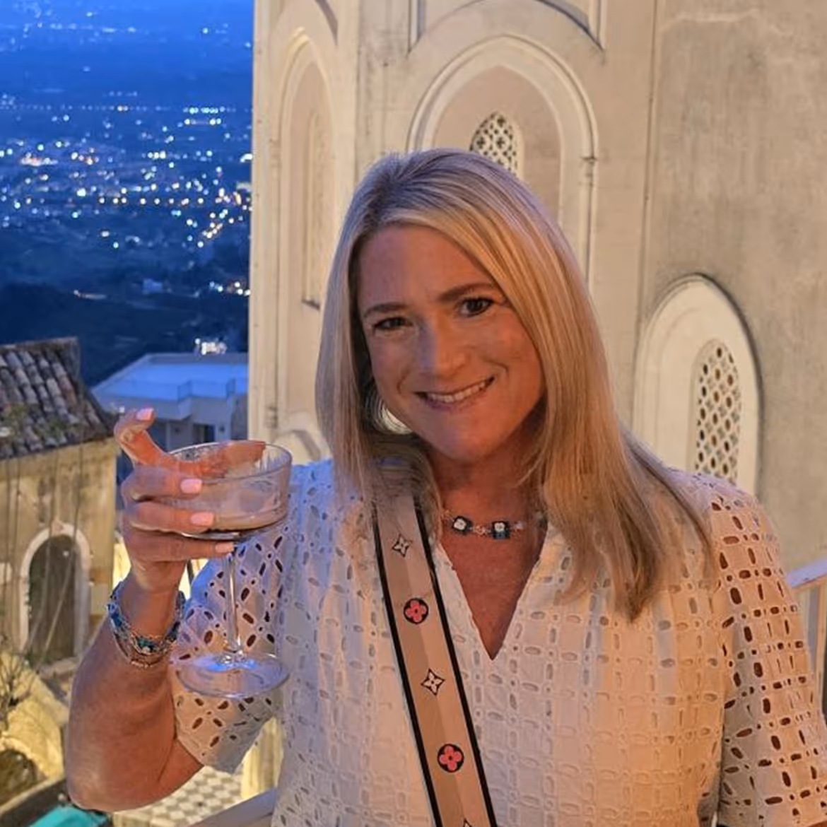 Woman in white lace top smiling and holding wine glass at night