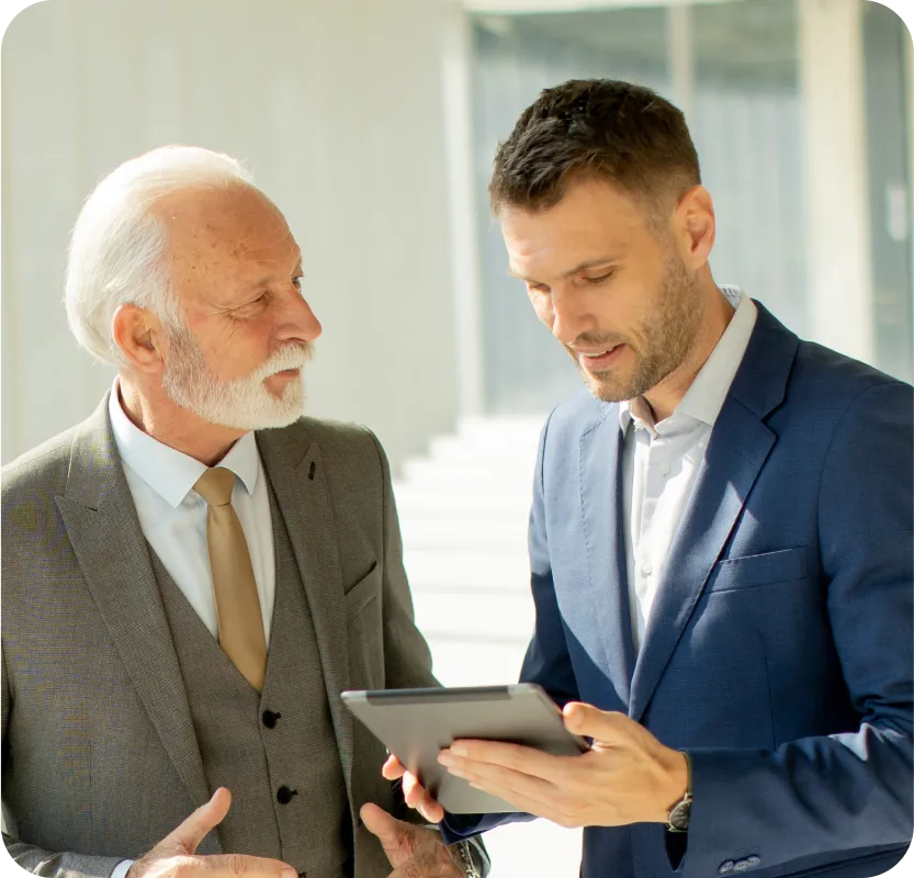 Two men in suits looking at a tablet.