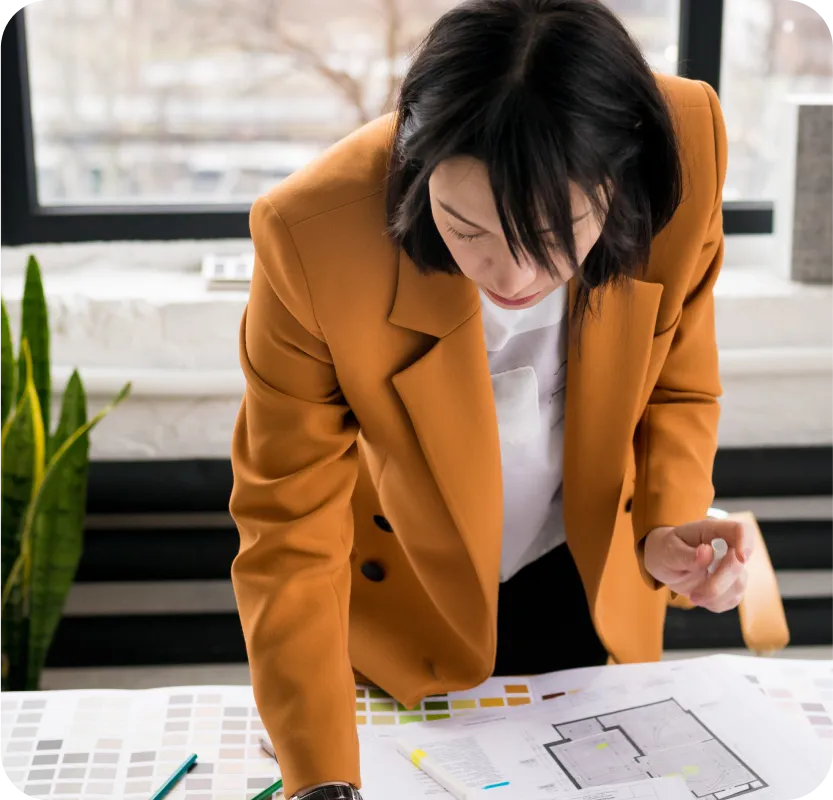 A woman in an orange jacket looking at a blueprint.