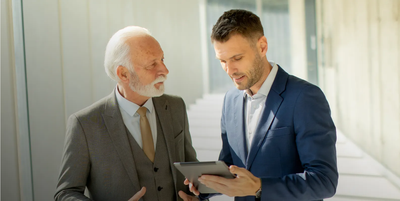Two men in suits looking at a tablet.