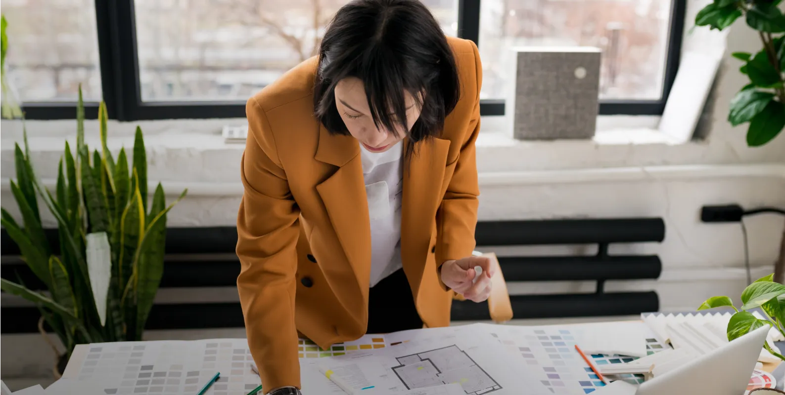A woman in an orange jacket looking at a blueprint.