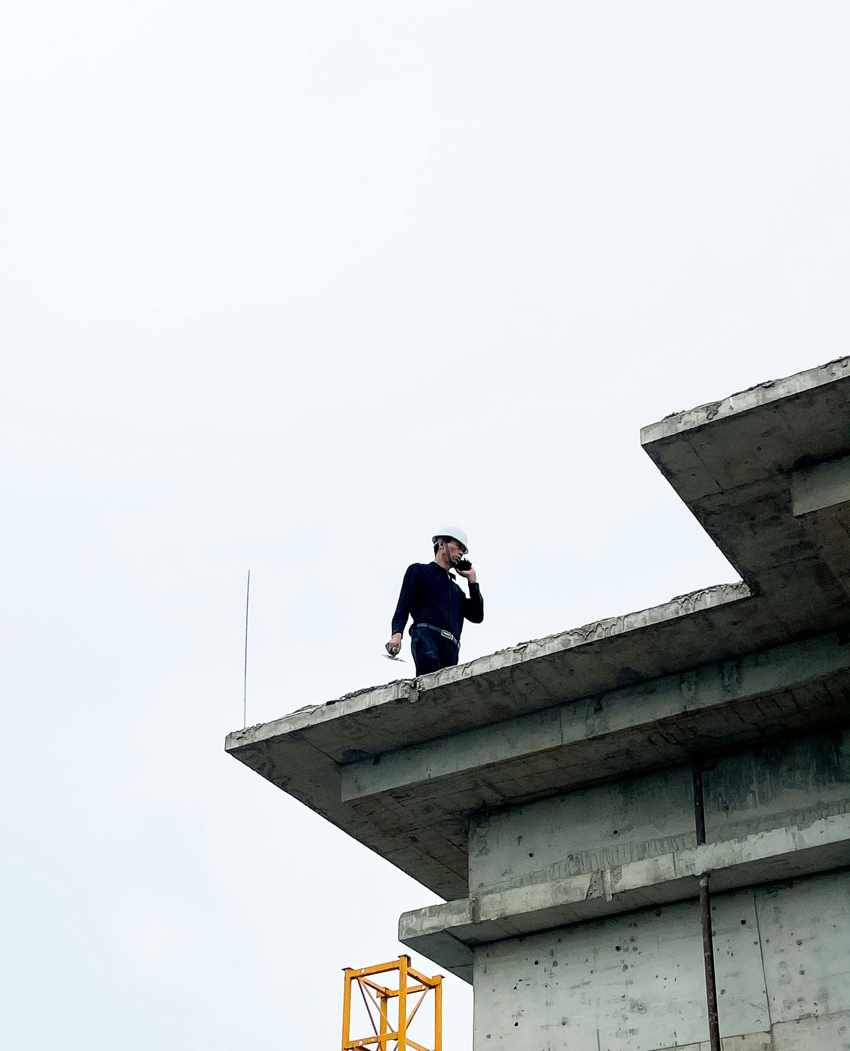 Jefe de obra con casco blanco hablando por teléfono en el borde de una losa en construcción