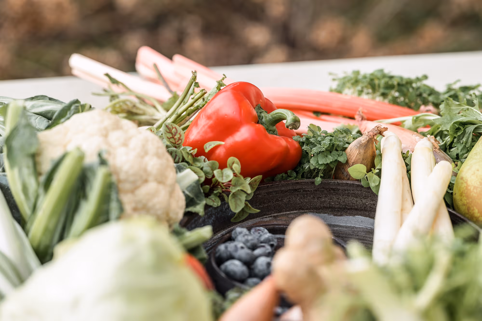 Verschillende verse groenten en fruit, waaronder een rode paprika, bloemkool, asperges en blauwe bessen in een schaal.