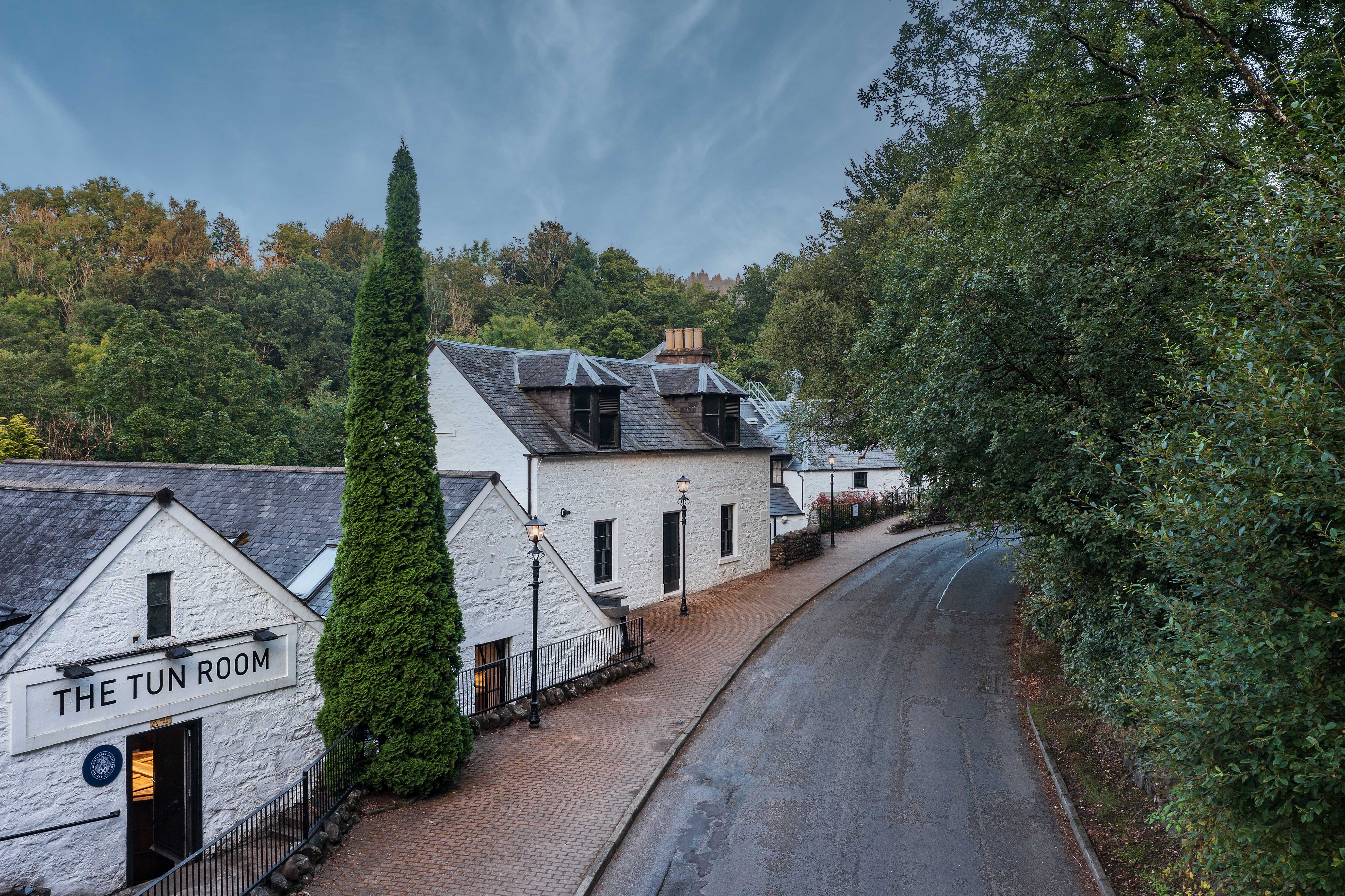 Jockey in racing gear riding a horse mid-jump over a fence at a racecourse with spectators and a grandstand in the background.
