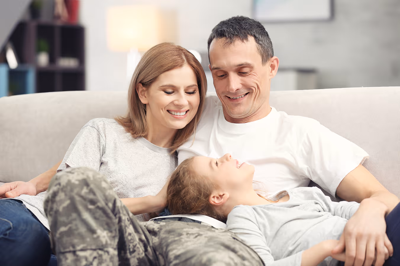 Smiling family with a man in military uniform, woman, and child sitting together on a couch.