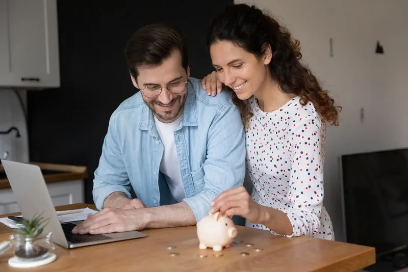 Smiling couple putting coins into a piggy bank at a table.