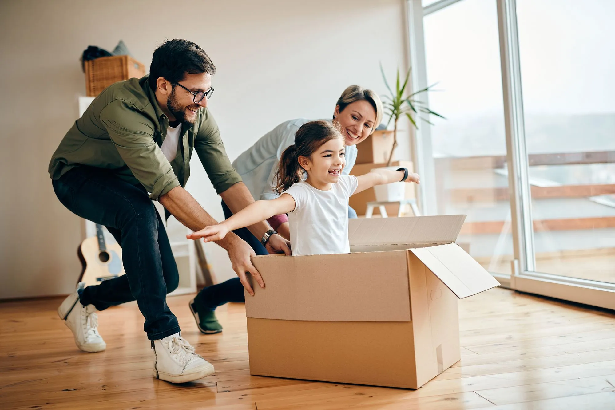 Happy family playing with a child inside a cardboard box in their new home.