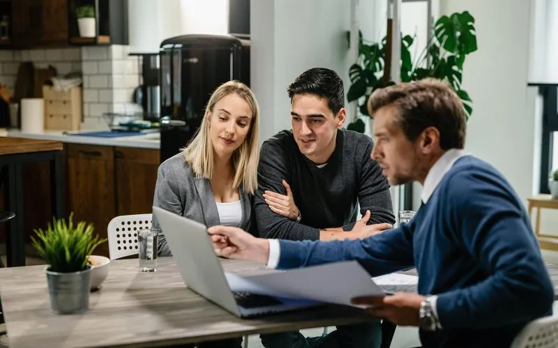 A mortgage agent showing details in his laptop to couple.
