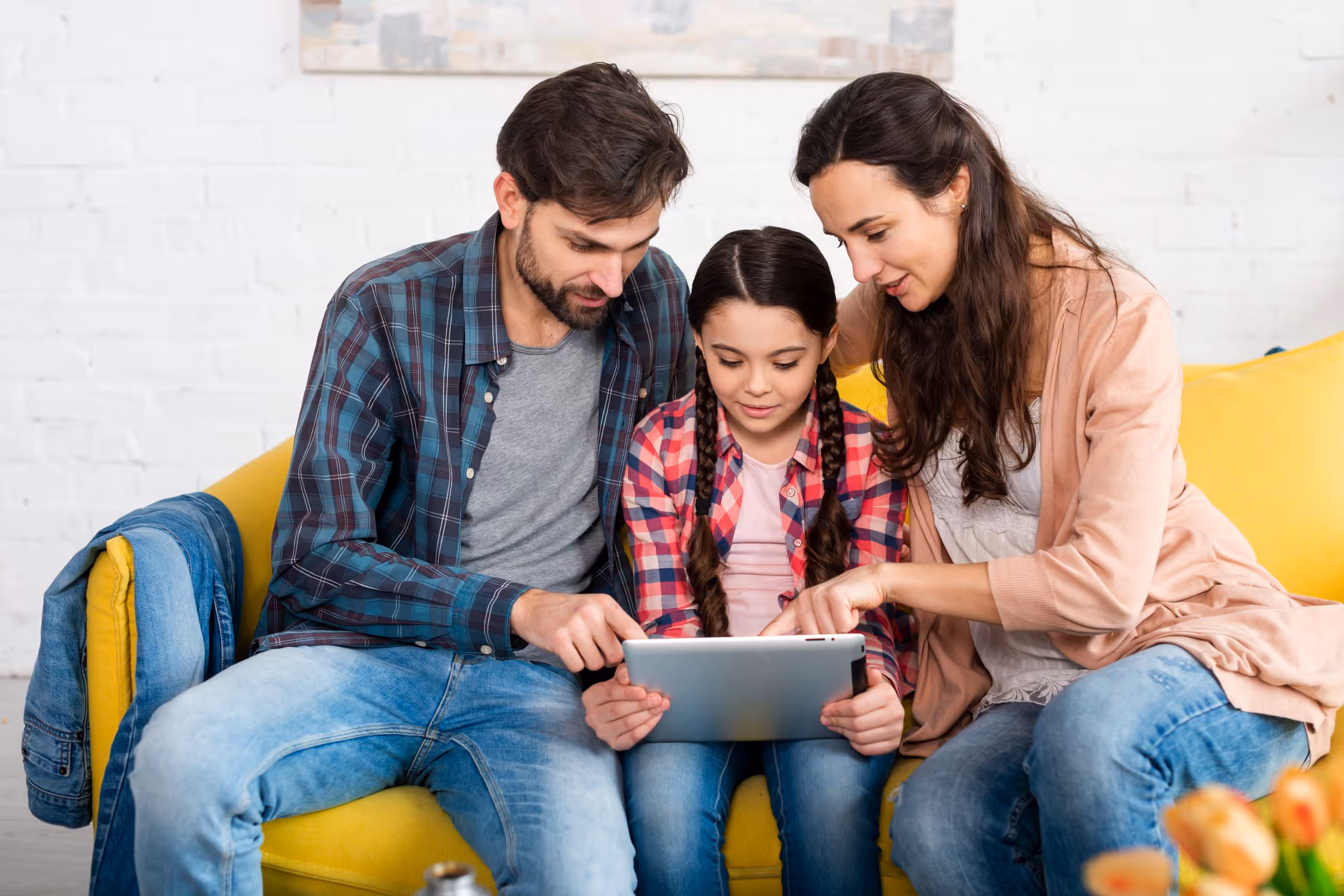 Happy family on yellow sofa inside their home watching tablet screen.