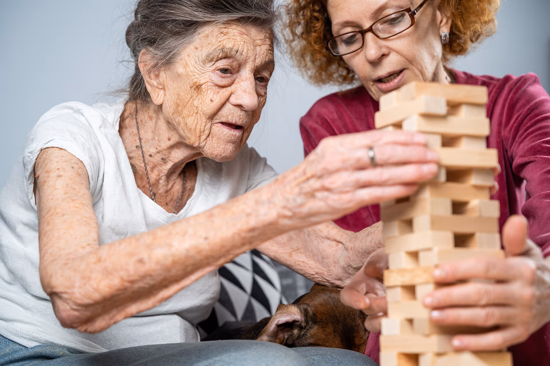 Deux femmes âgées jouent ensemble à un jeu de société en bois, concentrées sur la tour de blocs en bois.