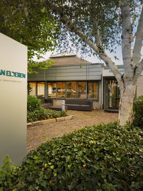 Moderne kantoorruimte met glazen ramen, omgeven door groen en een geklinkerde wandelweg.