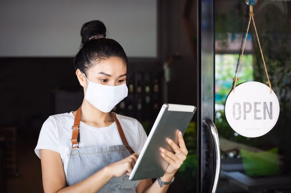 A woman wearing a face mask looking at a tablet.