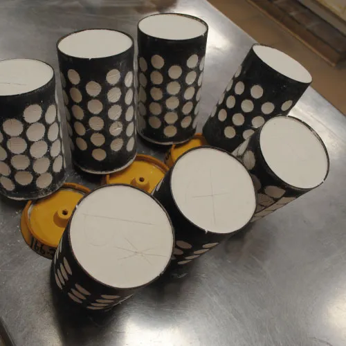 Six black cylindrical objects with white circular patterns arranged on a metallic surface.