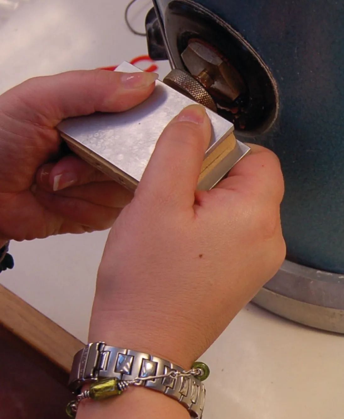 Close-up of hands holding a metal block near a rotating sharpening wheel.