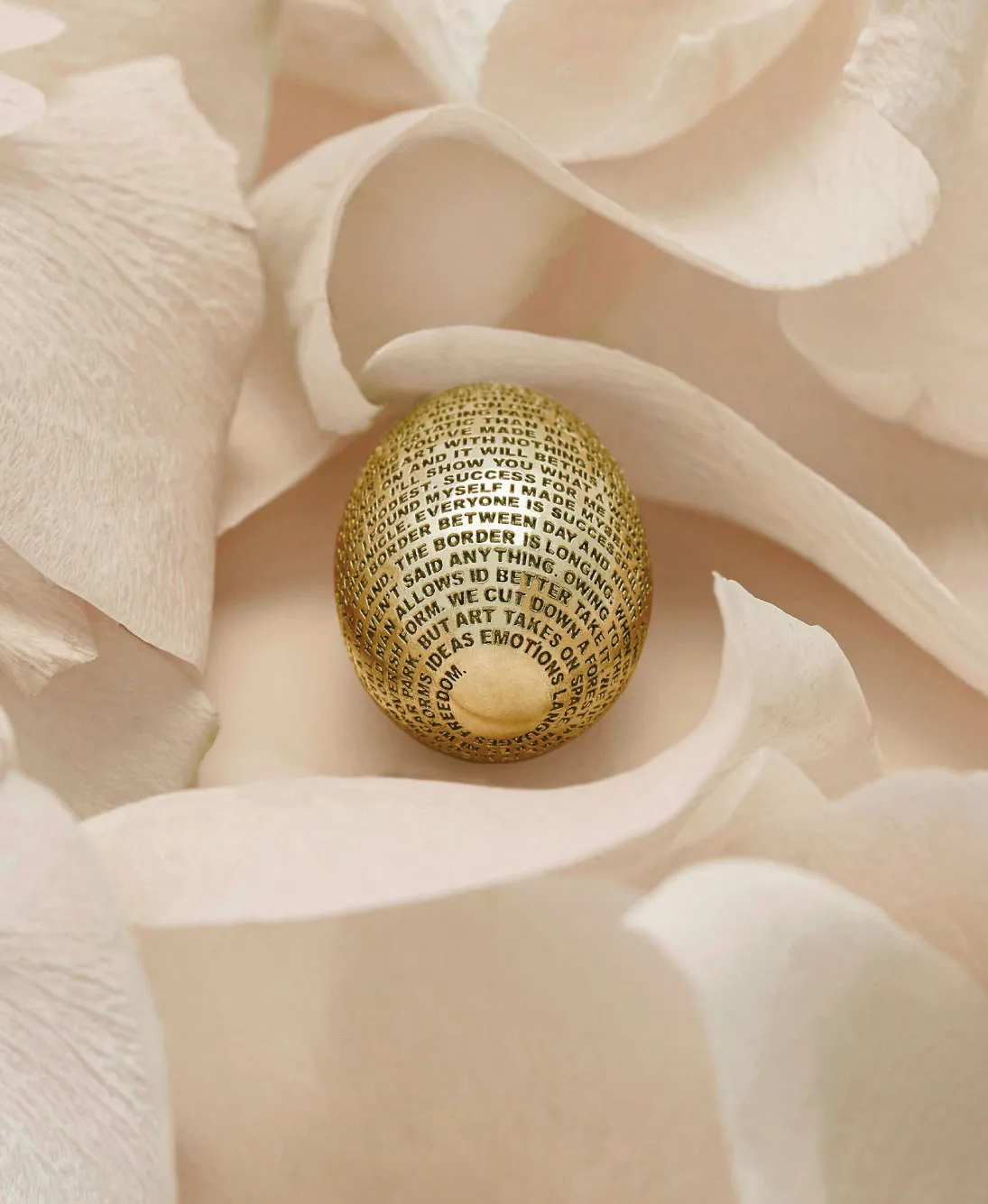Golden egg covered with black printed text nestled in soft, pale beige flower petals.