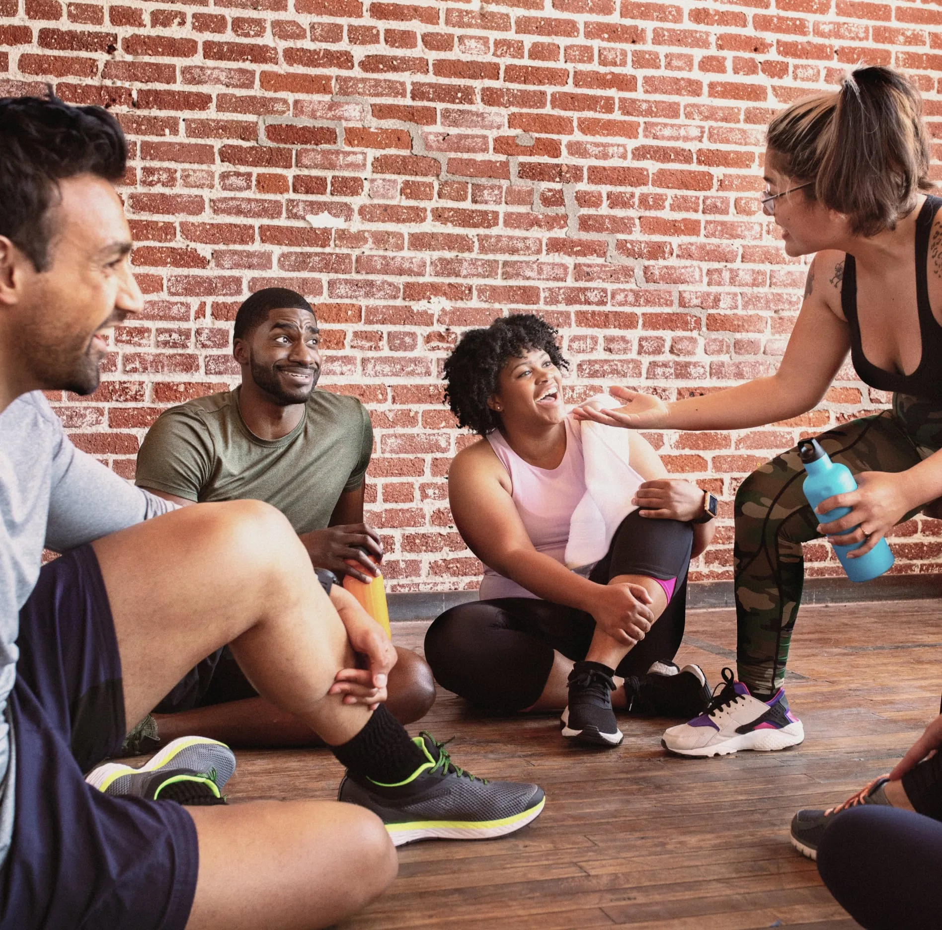 Group of diverse individuals sitting against a brick wall, participating in a lively, casual discussion.