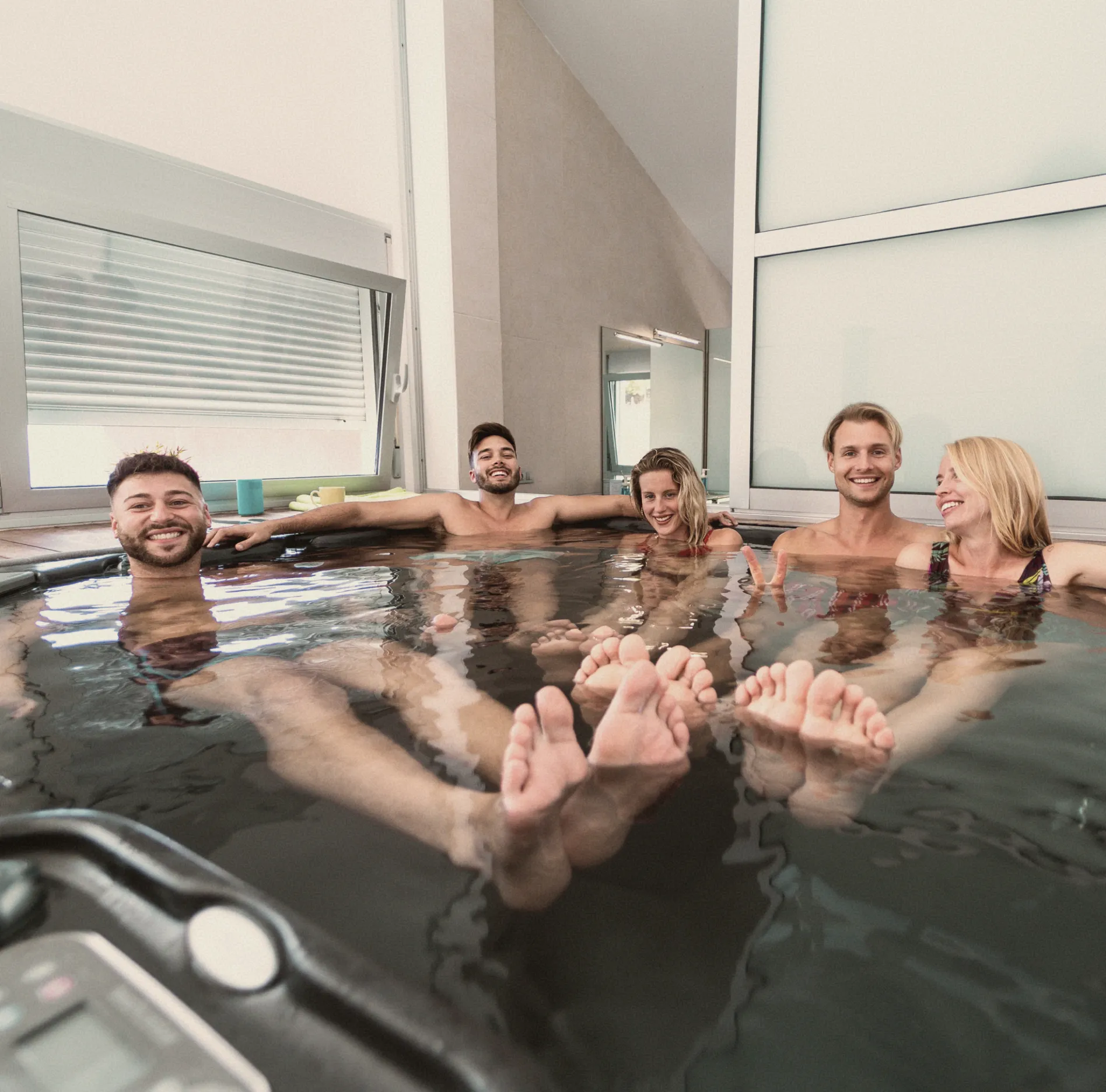 Group of people enjoying a communal spa experience in a hot tub inside a modern wellness center.