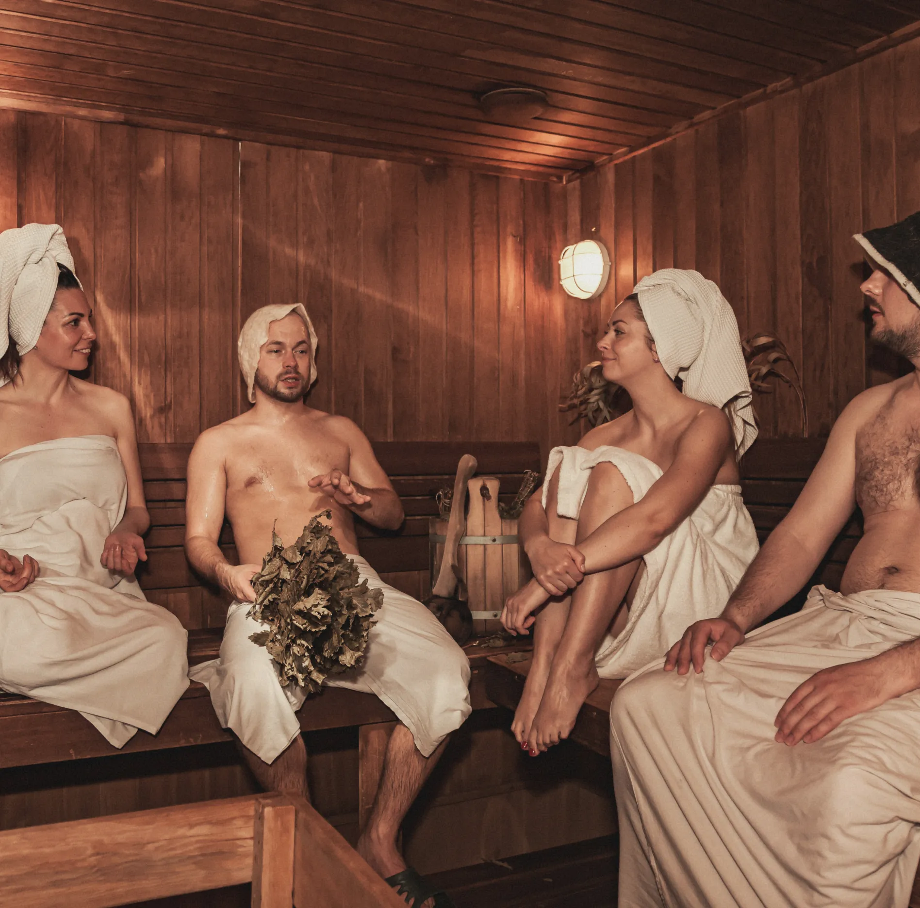 Artistic depiction of ancient Romans relaxing in a luxurious bathhouse, talking and lounging on benches.
