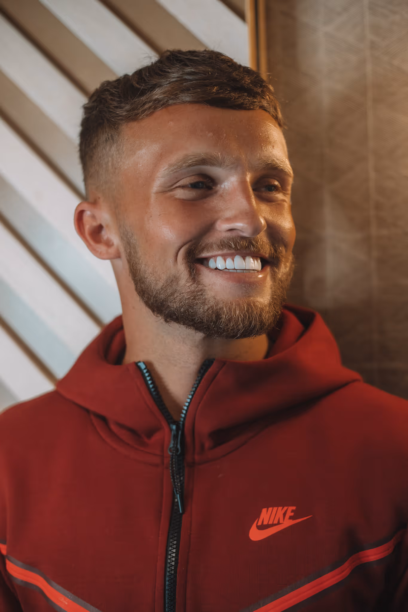 A man with a beard wearing a red nike hoodie, smiling.