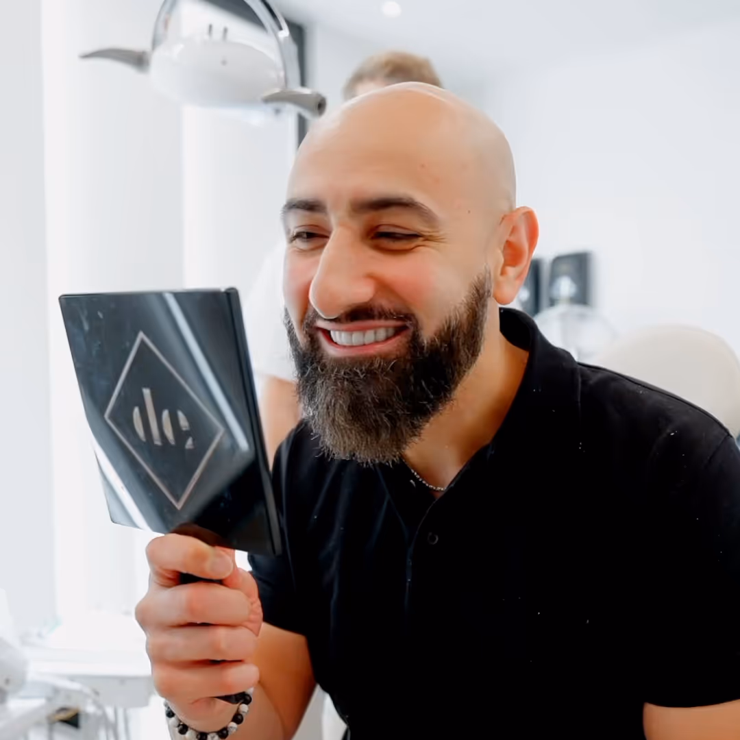 A man with a beard, smiling into a  hand held mirror.