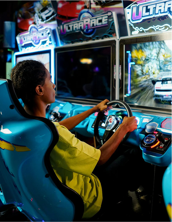 Young guy in front of a steering wheel at an arcade