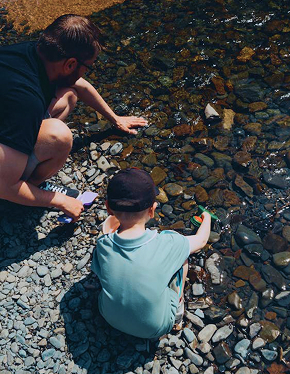 Father and son exploring a shallow clear lake with their hands