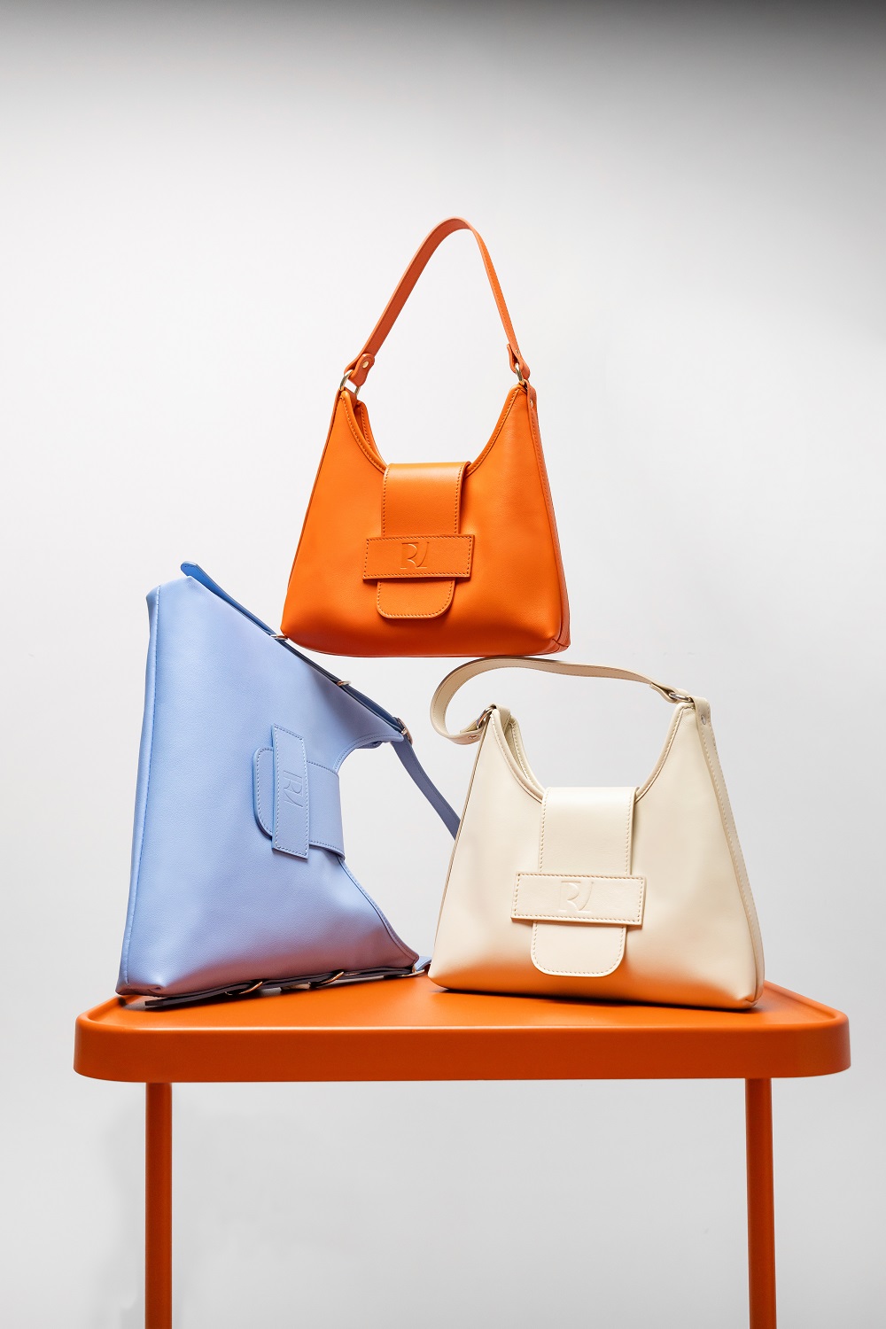 3 sacs a main Fada posés sur une table : un orange, un bleu et un jaune pale