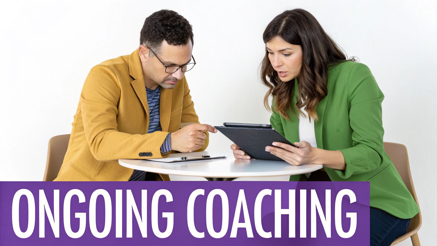 Two professionals, a man and a woman, engaged in an ongoing coaching session, looking at a tablet.