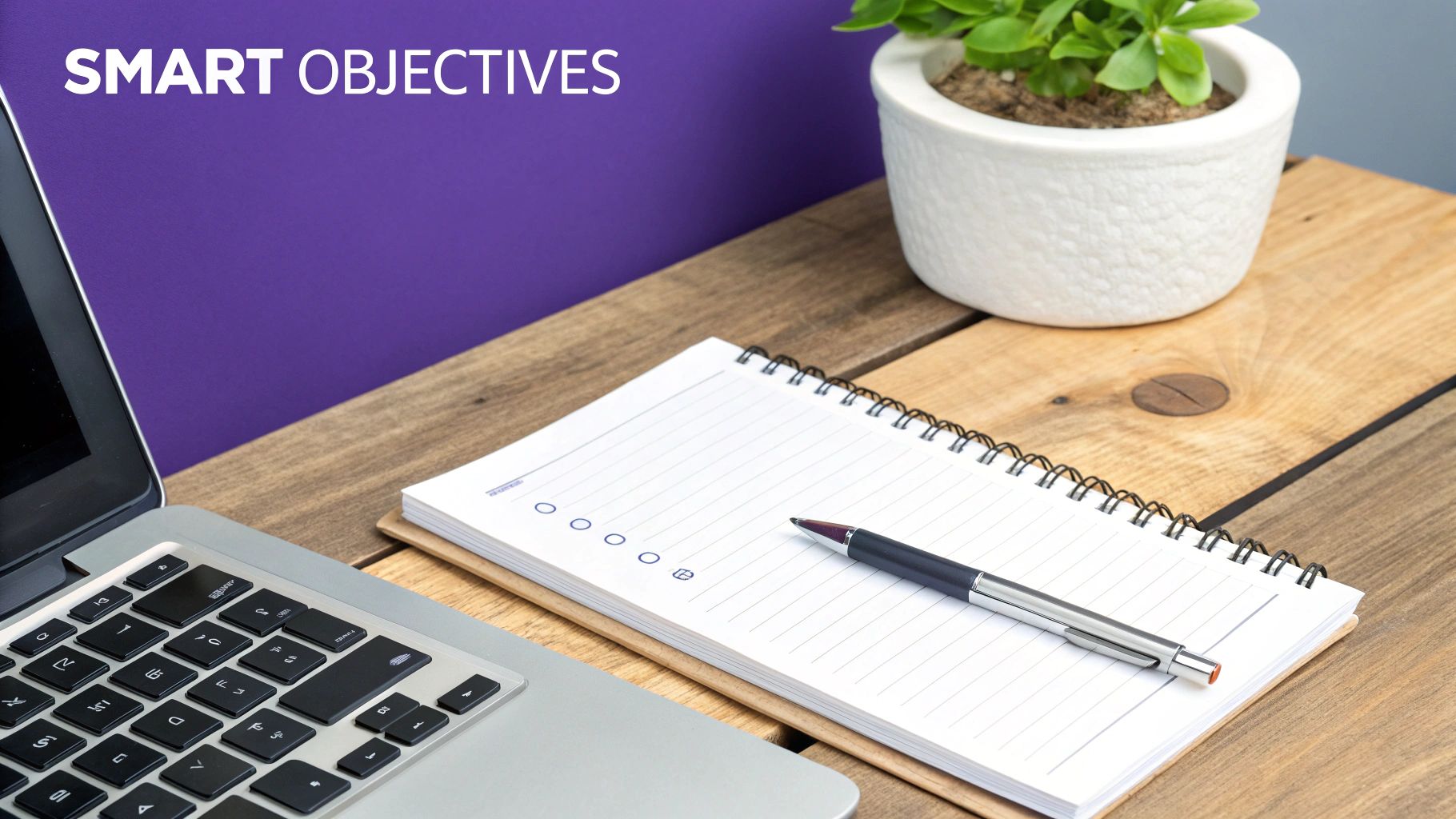 A desk with a laptop, a spiral notebook, and a pen, with "SMART OBJECTIVES" on a purple wall.