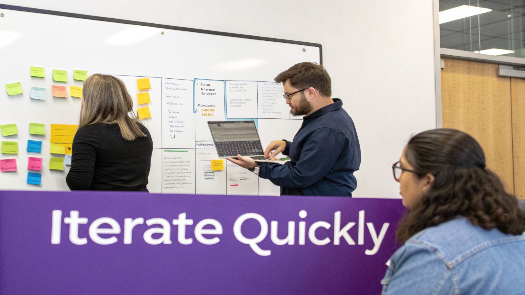Team members collaborate during a brainstorming session, using a whiteboard with sticky notes and a laptop.