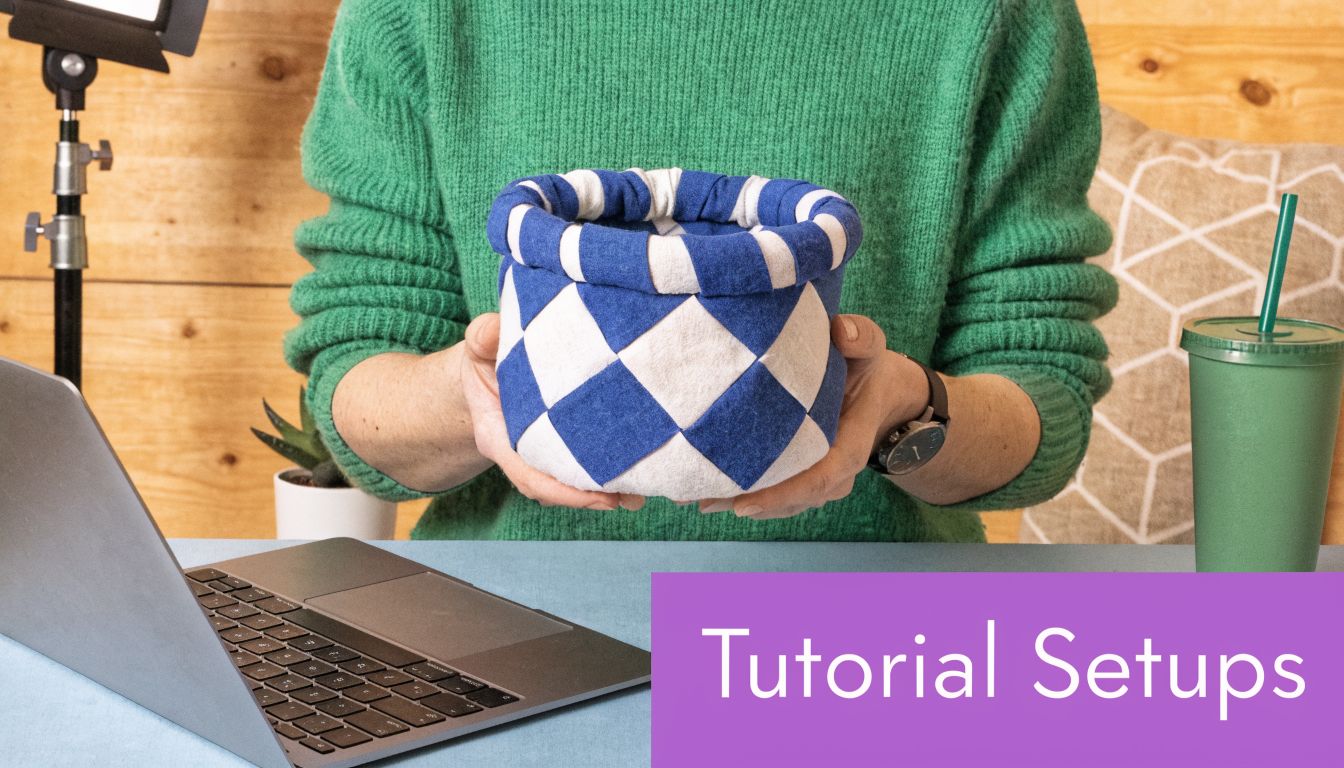 A person in a green sweater holding a blue and white woven craft basket in front of a laptop.