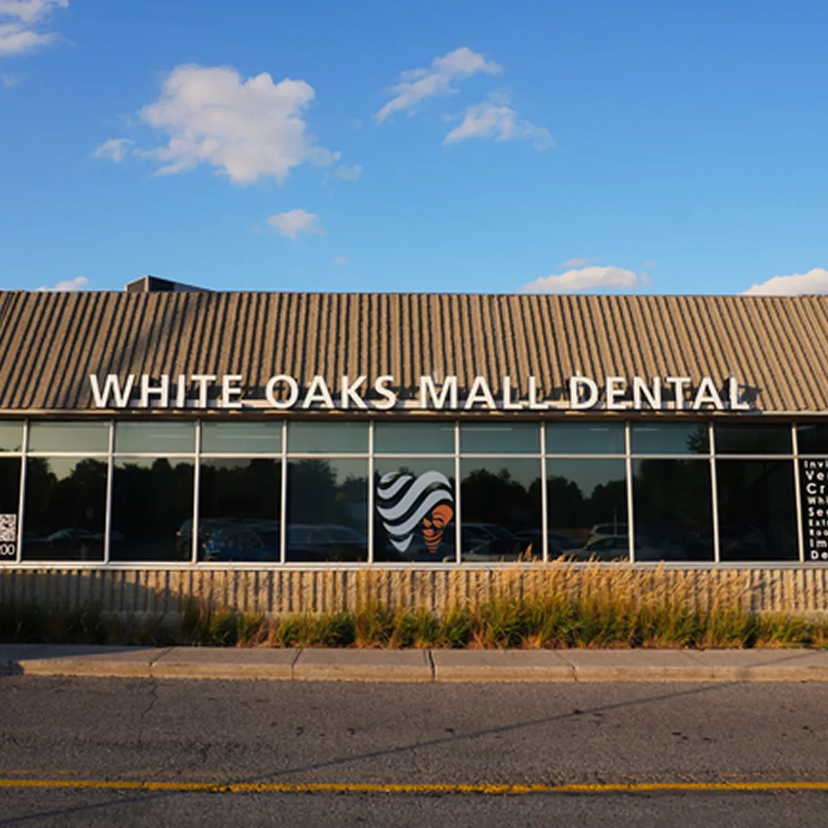 Exterior of White Oaks Mall Dental with a sign on the roof and a window displaying a stylized face logo.