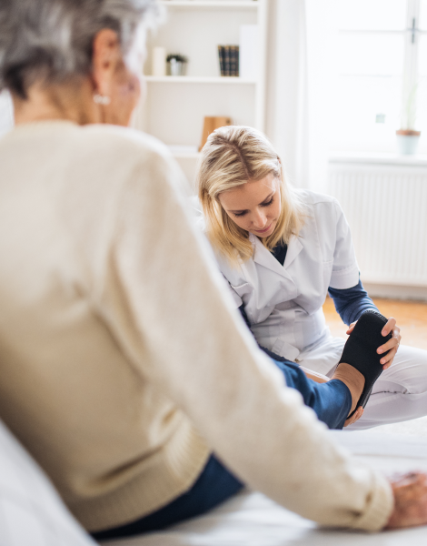 Eine medizinische Fachkraft untersucht den Fuß einer älteren Frau in einem hellen Zimmer.