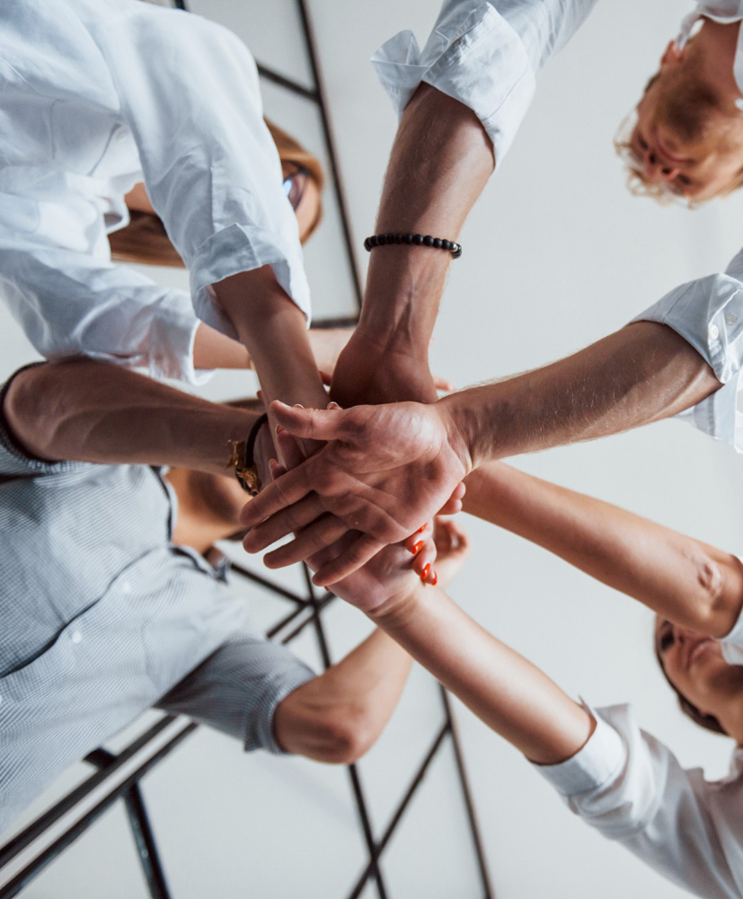 Mehrere Menschen legen im Stehen ihre Hände übereinander als Zeichen von Teamwork.