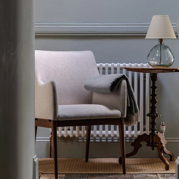 Cozy reading nook featuring a gray chair, wooden side table and elegant glass lamp.
