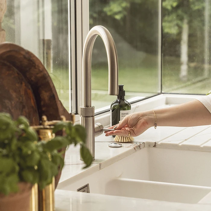 Cleaning dishes with soap and brush under a stainless steel kitchen faucet.