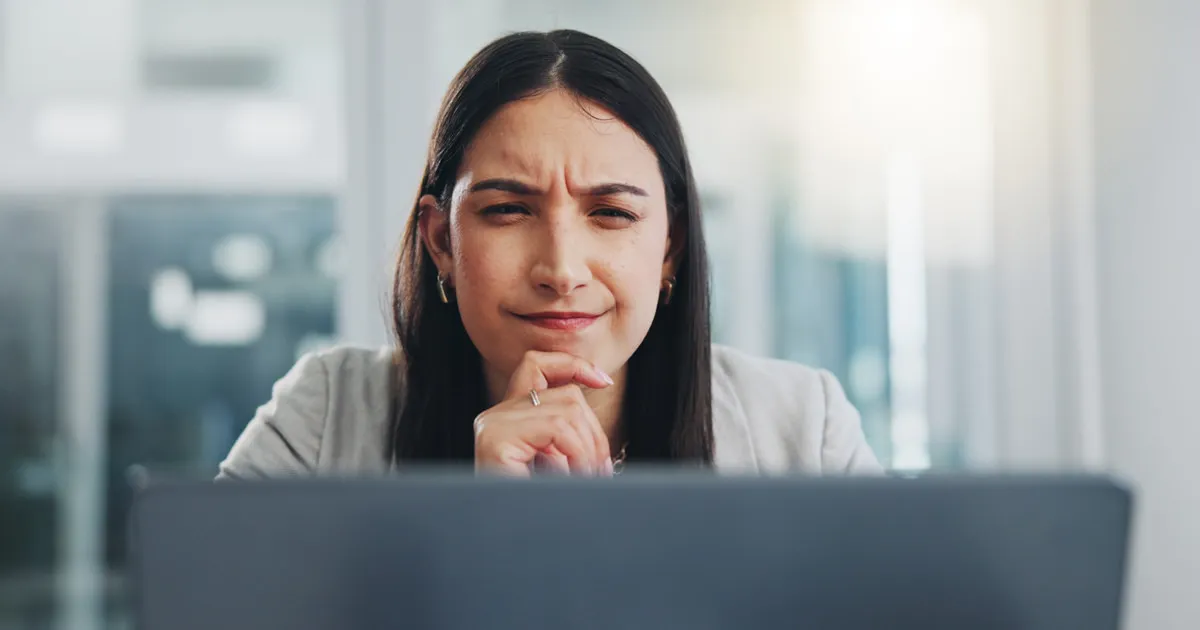 A woman in front of a computer notebook with a facial expression of someone thinking.