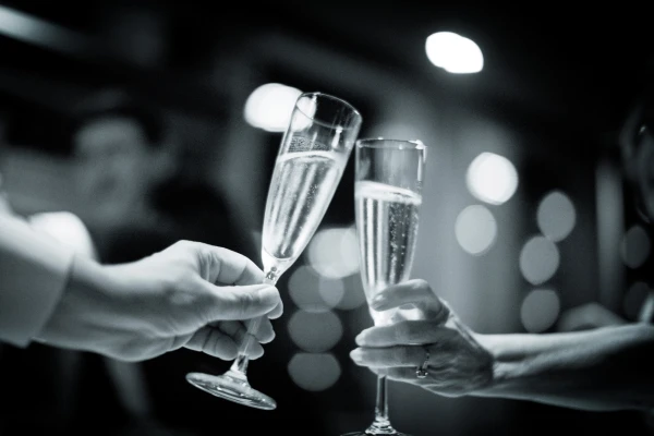 Zwei Hände stoßen mit Champagnerflöten in einer Feier mit unscharfem Hintergrund an.